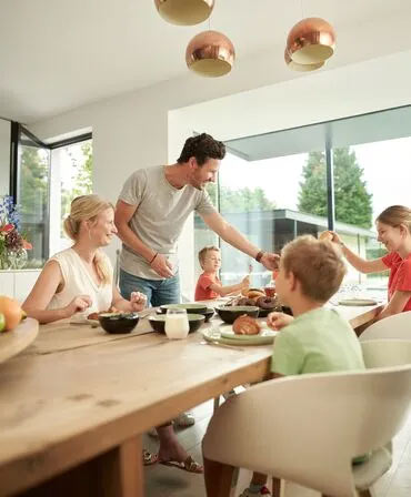 family enjoying a meal together, with natural light streaming in through ConceptSystem 77 windows